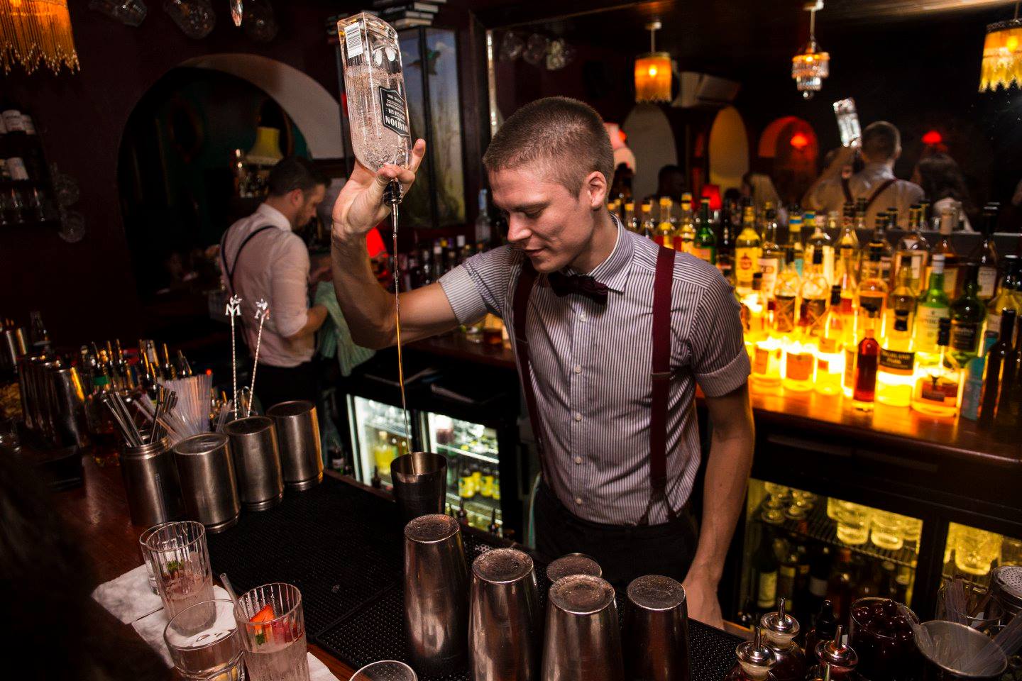 A bartender in bow tie and braces pours a spirit into a mixing glass behind the bar at Hyde and Co, named one of Bristol's Best Bars by The Cocktail Society