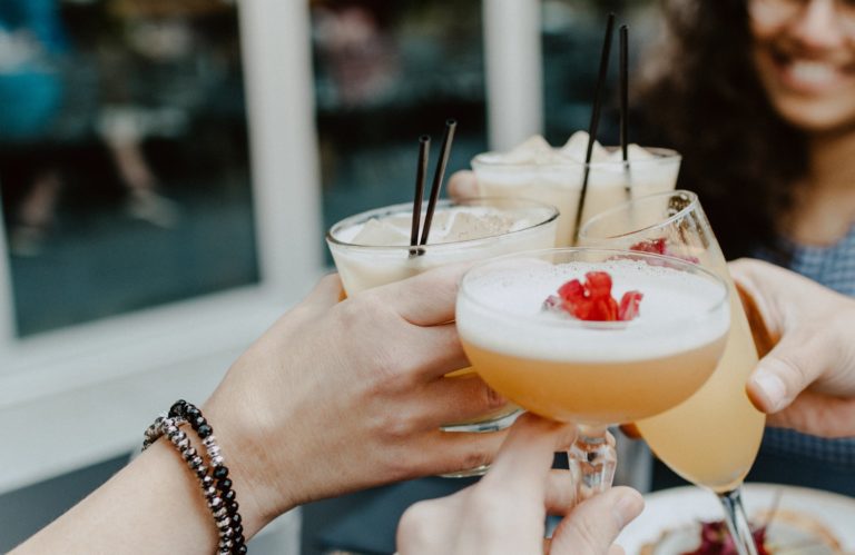 People holding cocktails - french martini and long island iced tea, saying cheers. The best summer cocktails -Photo by Kelly Sikkema on Unsplash