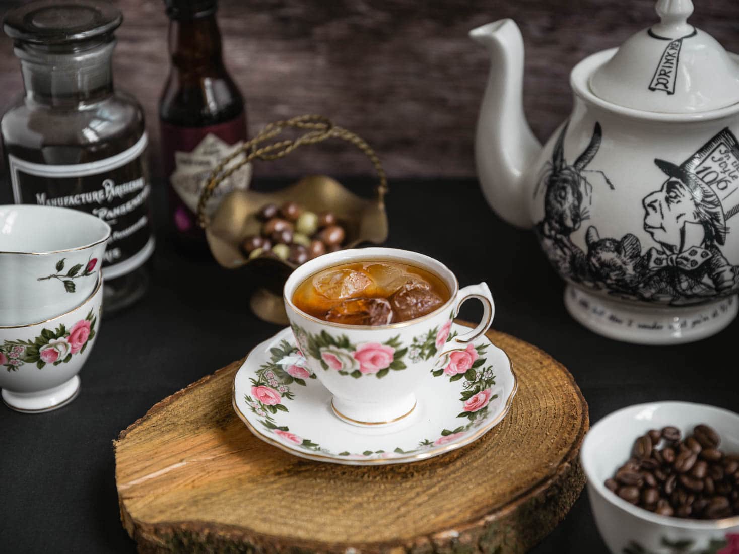 A china tea cup with floral pattern, containing a dark cocktail, sitting on a wooden board, in front of a teapot and bowl of olives - from the Clockwork Rose bar Bristol