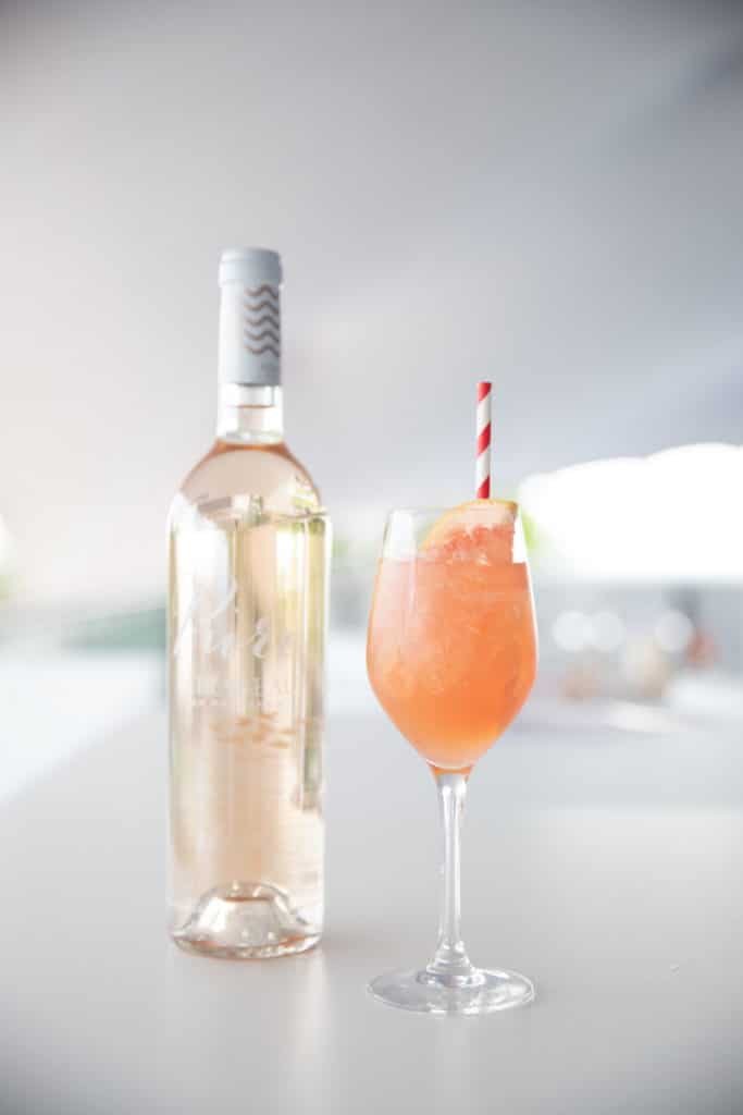 Provence Spritz Rosé Cocktail using Mirabeau Pure Rosé in a wine glass, with a bottle of Mirabeau Pure Rosé in the background.