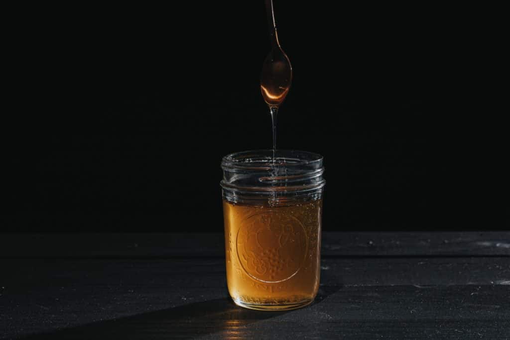 A jar of sugar syrup with syrup dripping from a spoon