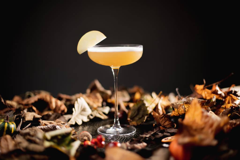 A Toffee Apple Martini created by The Cocktail Society in a bed of Autumn leaves