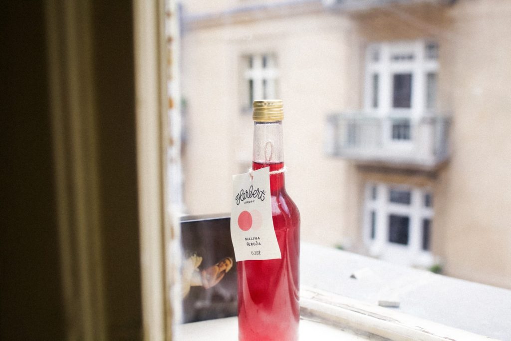 A bottle of red cocktail shrubs made with strawberries by a window