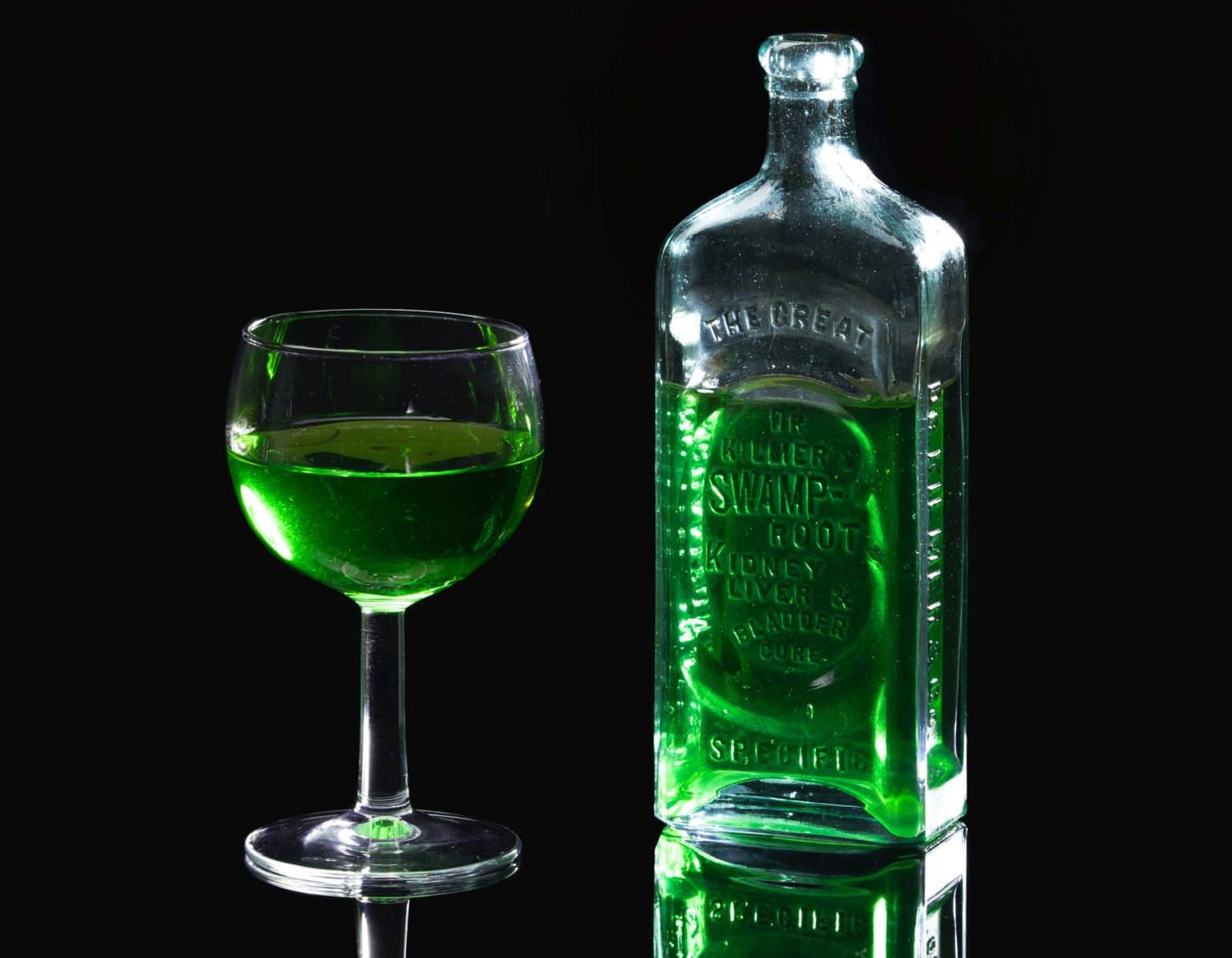 A green cocktail from a list of Absinthe cocktail recipes next to a bottle of green Absinthe