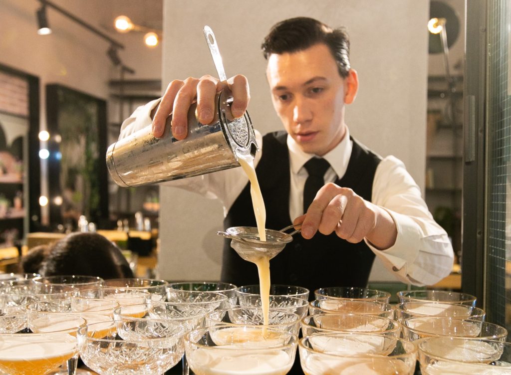 A bartender at a masterclass pours a drink showing guests when to shake a cocktail in a cocktail shaker