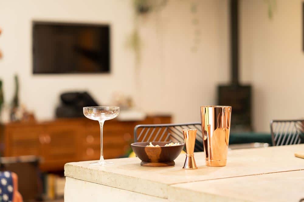 A coupe glass, cocktail shaker and jigger on a home bar